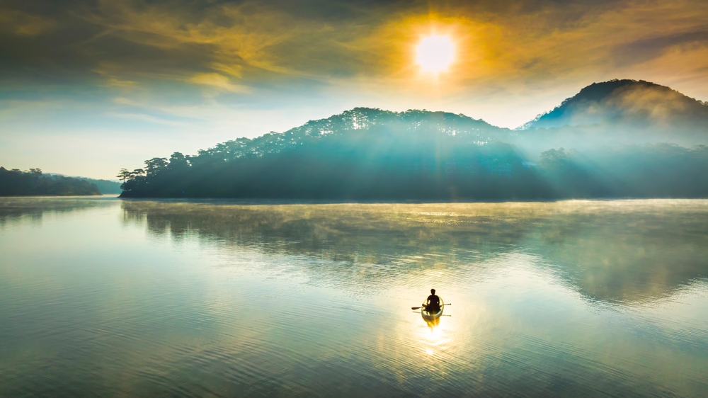 Die Morgensonnenaufgänge im Tuyen Lam See von ​Da ​, Vietnam. Die Sonne scheint durch die Pinienberge auf die ruhige Seeoberfläche, es ist wunderbar, sich zu entspannen und den morgendlichen Sonnenaufgang hier zu beobachten.
